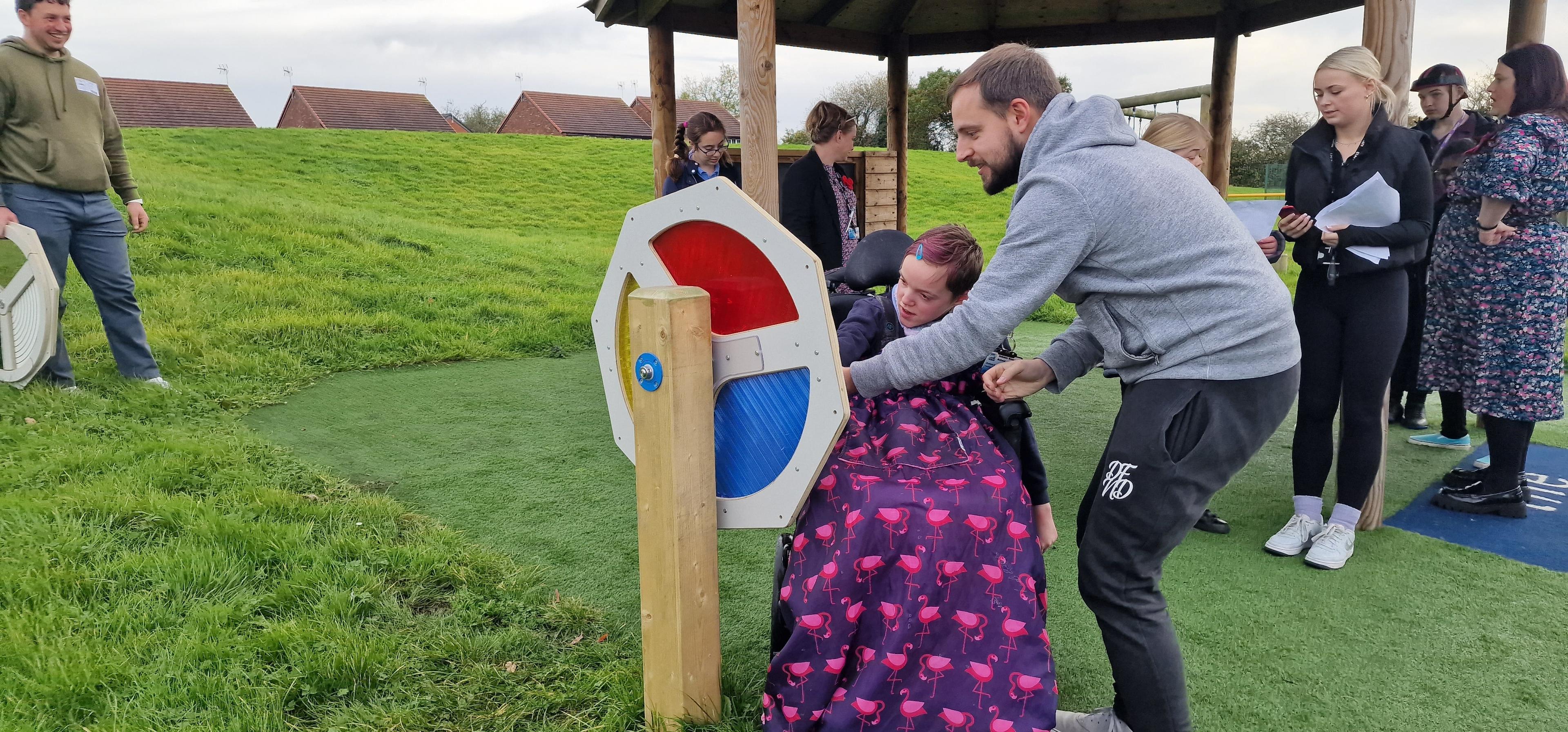 A girl in a wheelchair is being helped by a man to watch the Light Sensory Spinner.