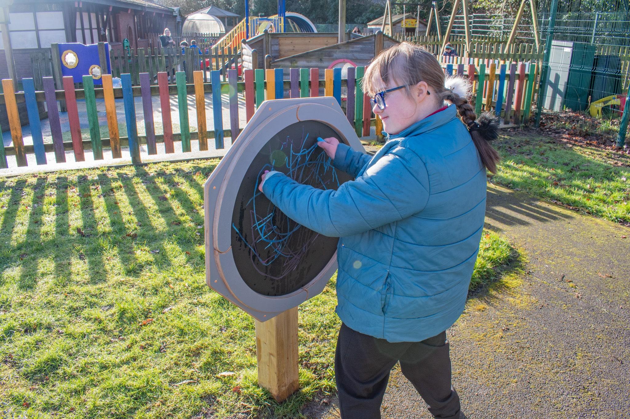 A girl with additional needs is drawing on the Drawing Sensory Spinner with blue chalk.
