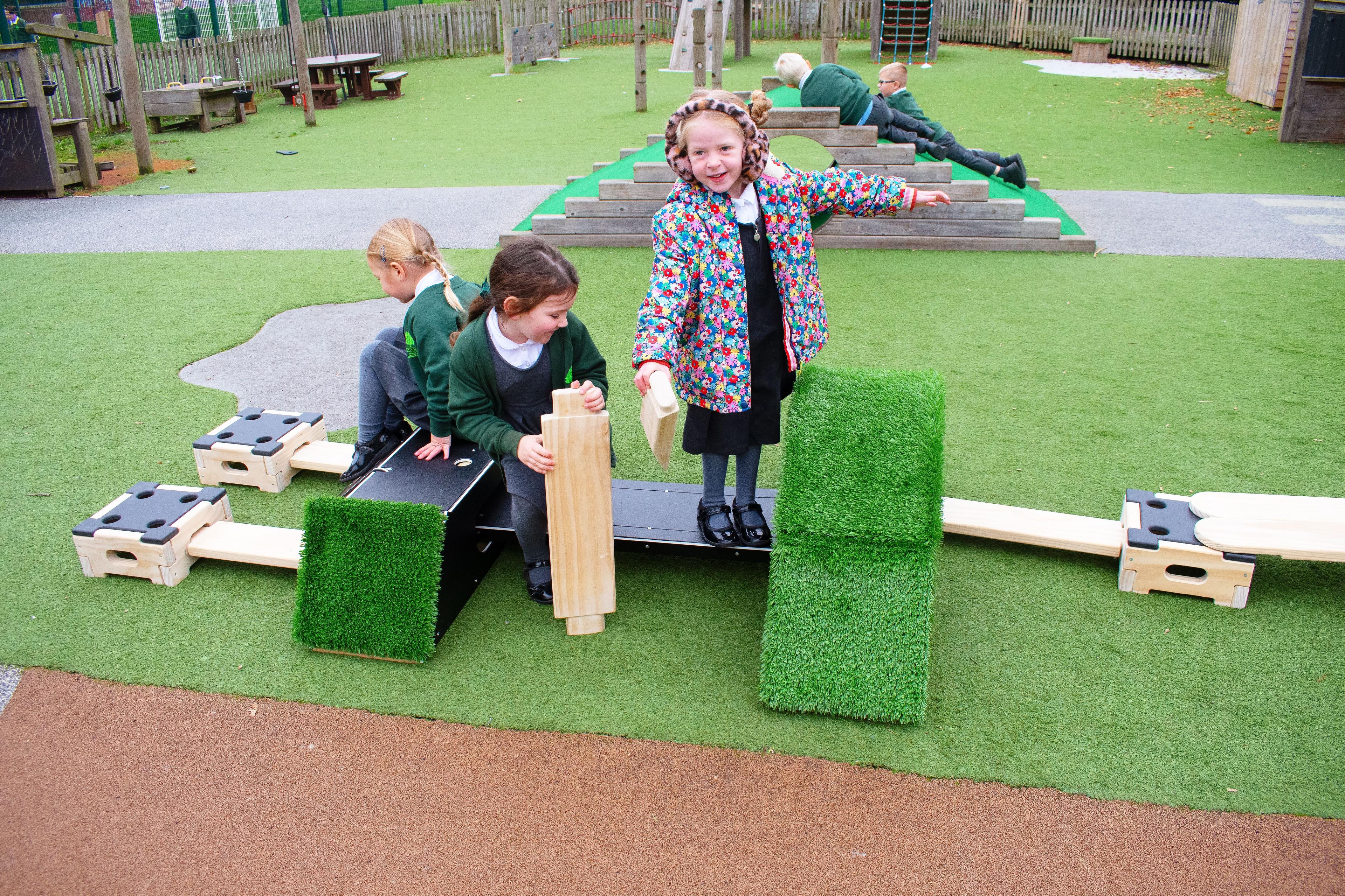 Three girls are attaching Play Builder planks to the Rockies to create a physical development circuit.