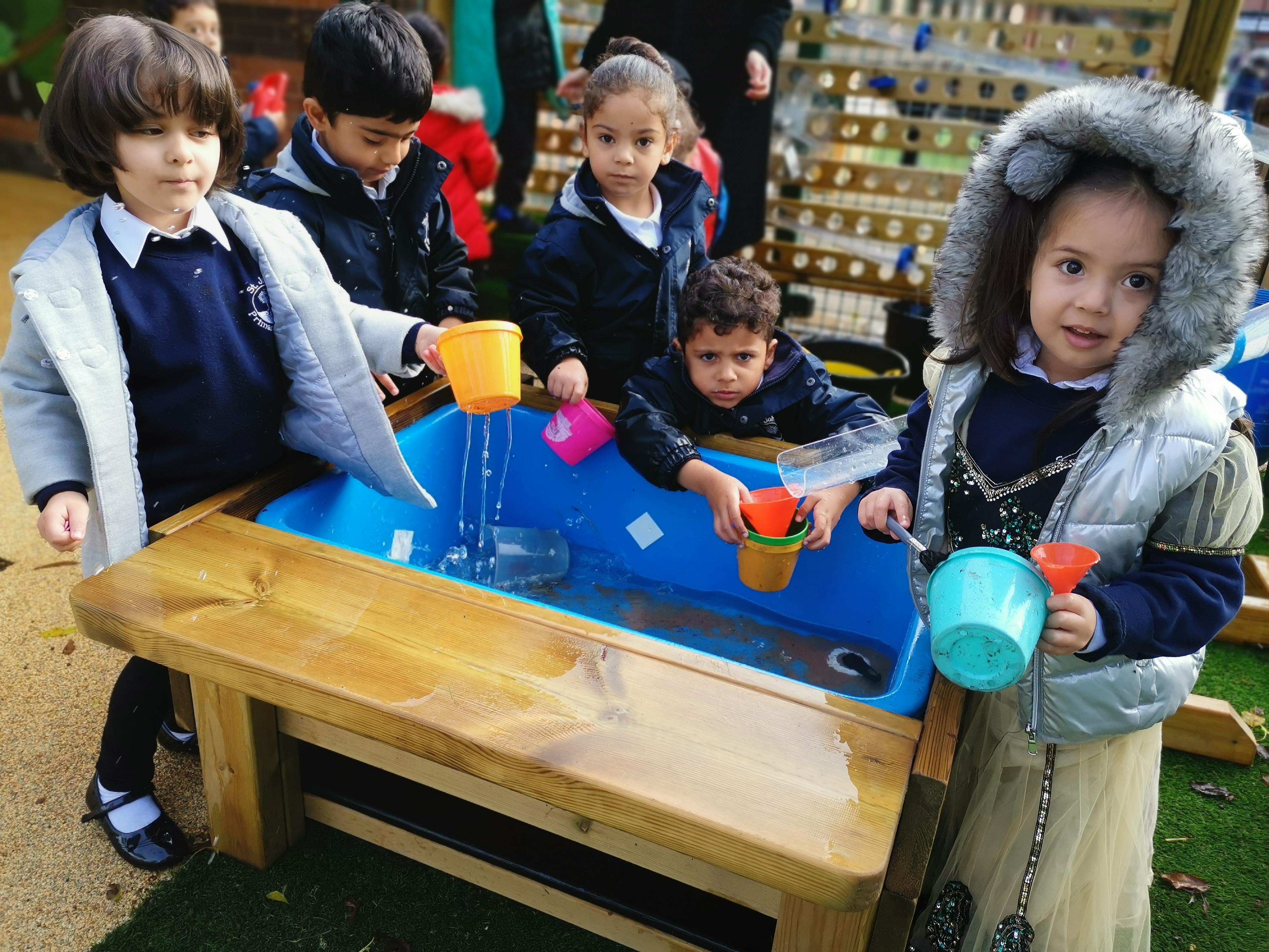 A group of children gathered around the water table that is part of the Water Wall with Water Play Package