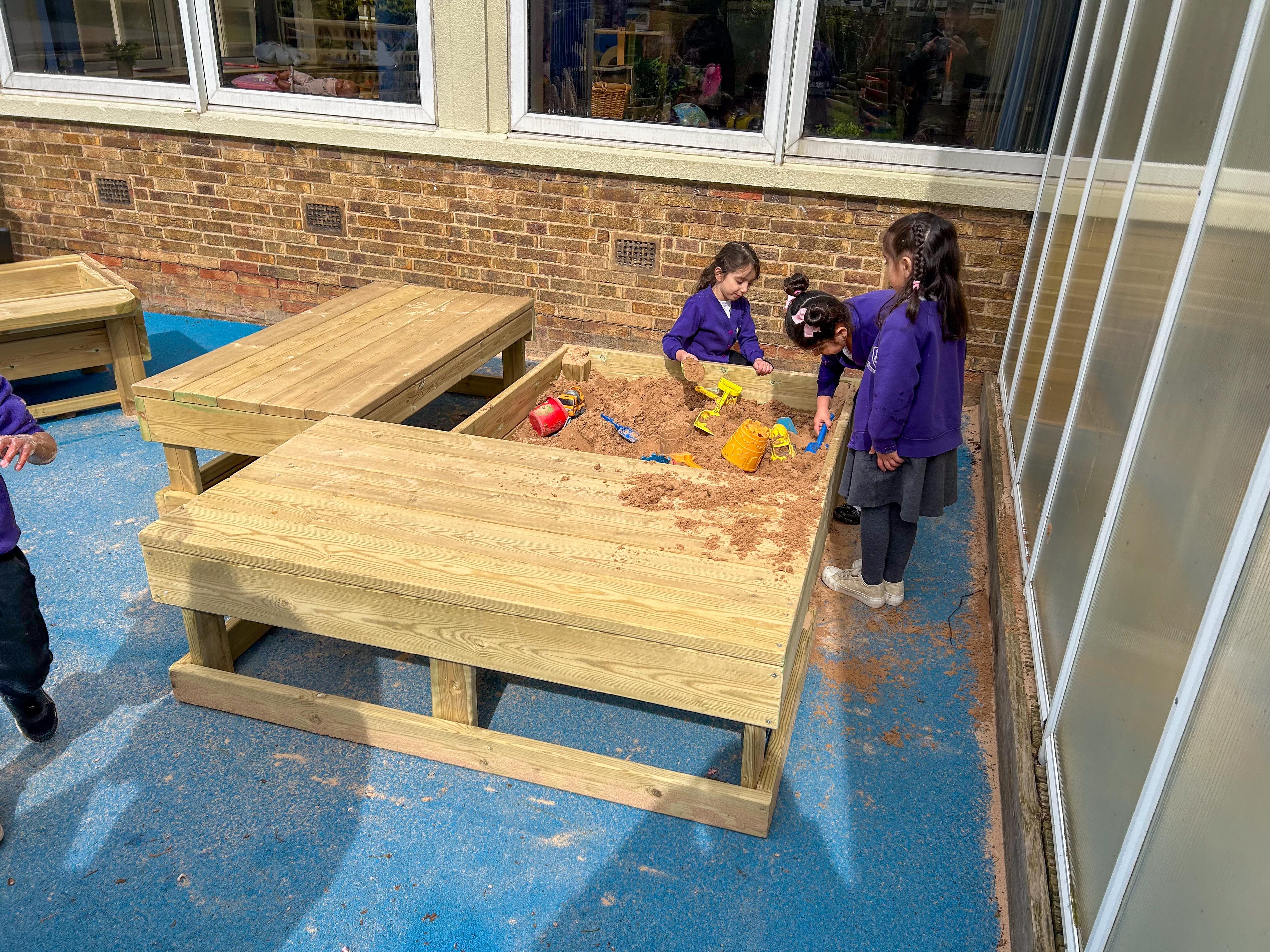 Three children are playing together as they stand outside the Small Covered Sand Box.