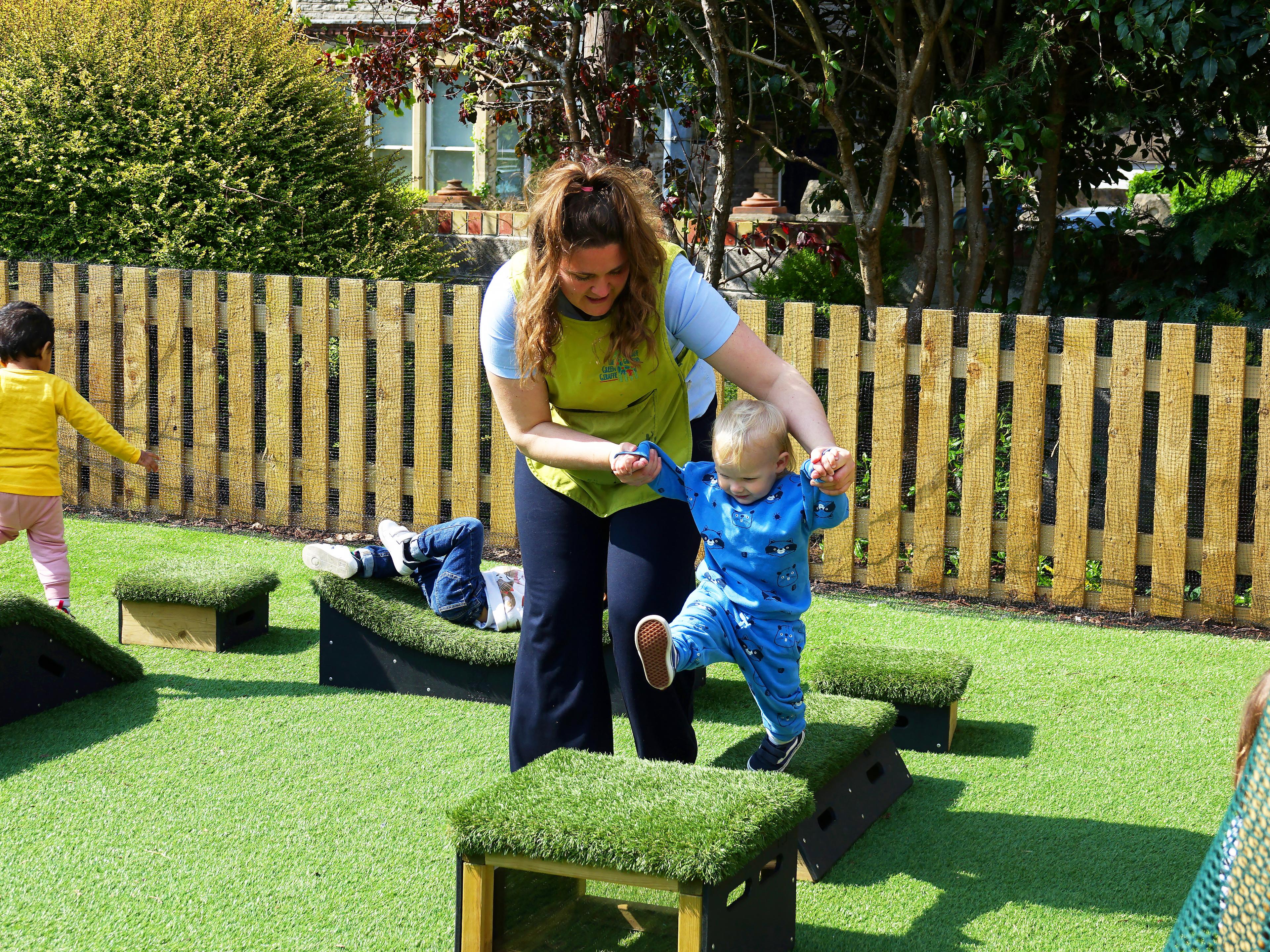 A female member of staff helping a small child get from one block to another