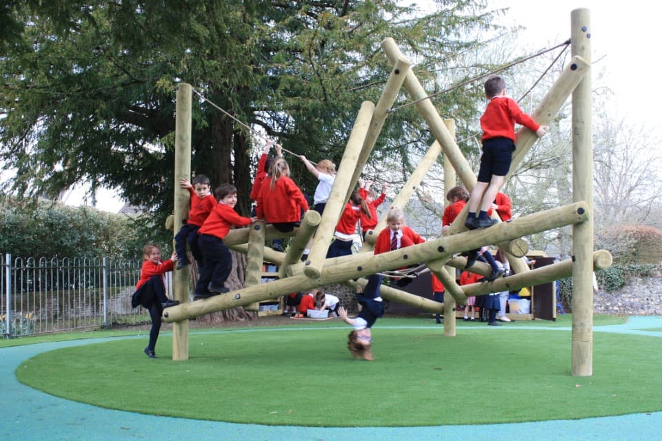 A group of wooden poles have been placed at different angles, with rope connecting between random logs. This structure creates a Playframe, which currently has children climbing all over it!