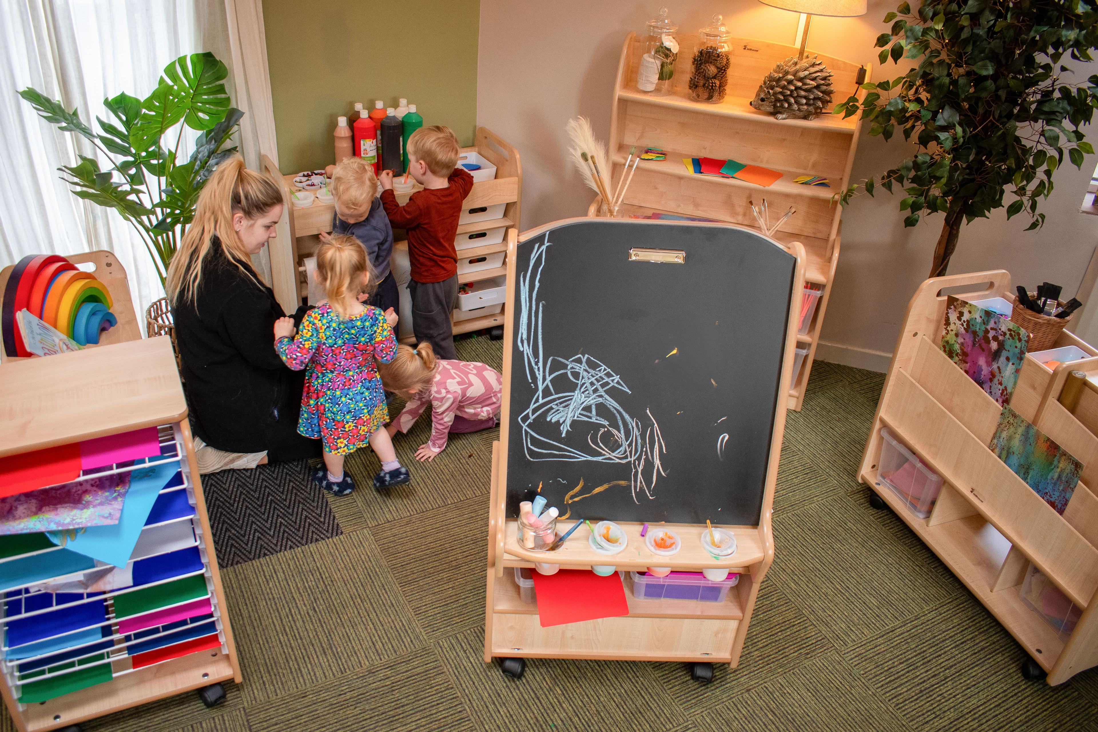 A classroom with a variety of arts and crafts furniture, with a group of children and teacher engaging with it.