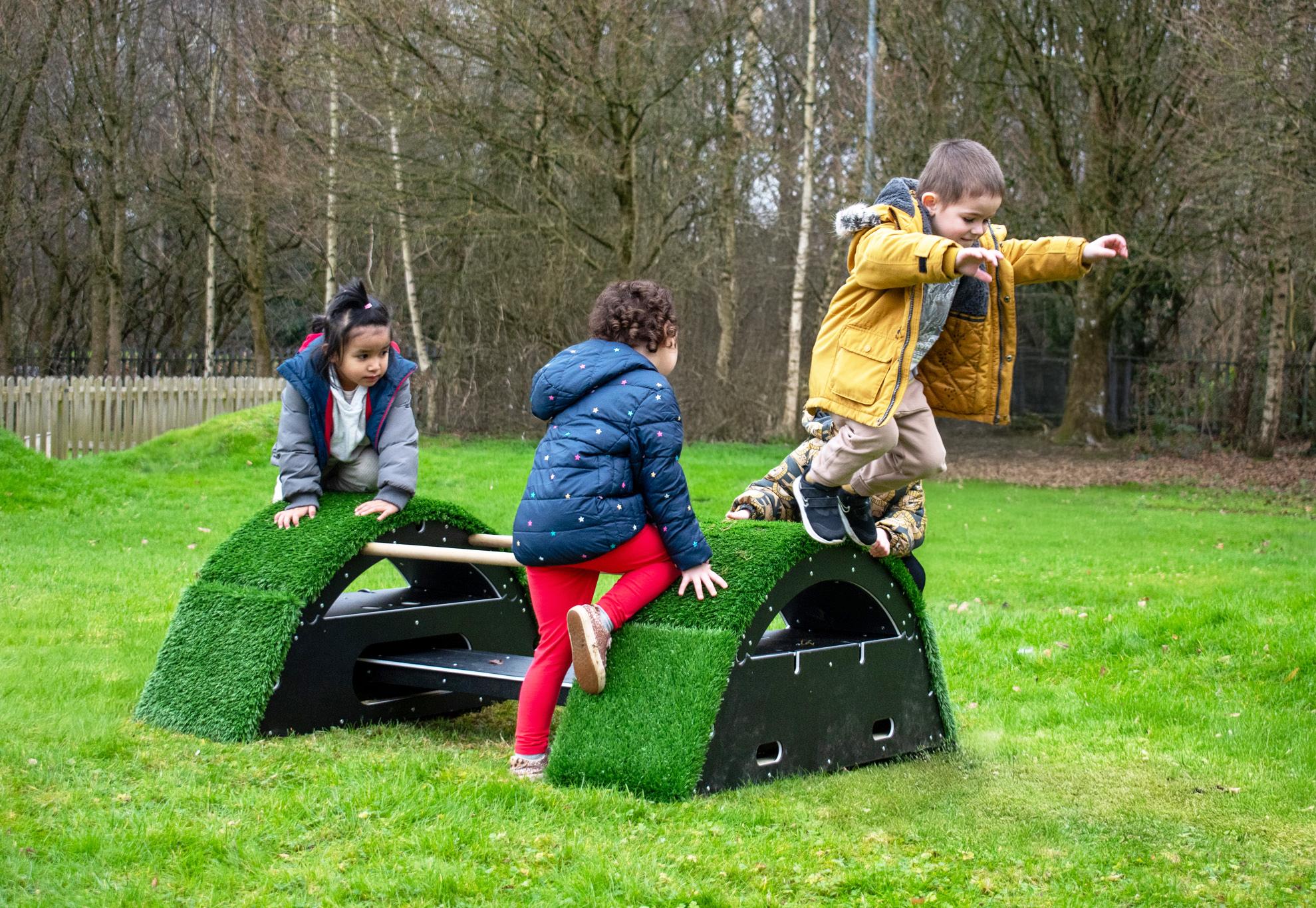 Three children playing and jumping on grass-topped blocks, The Rockies