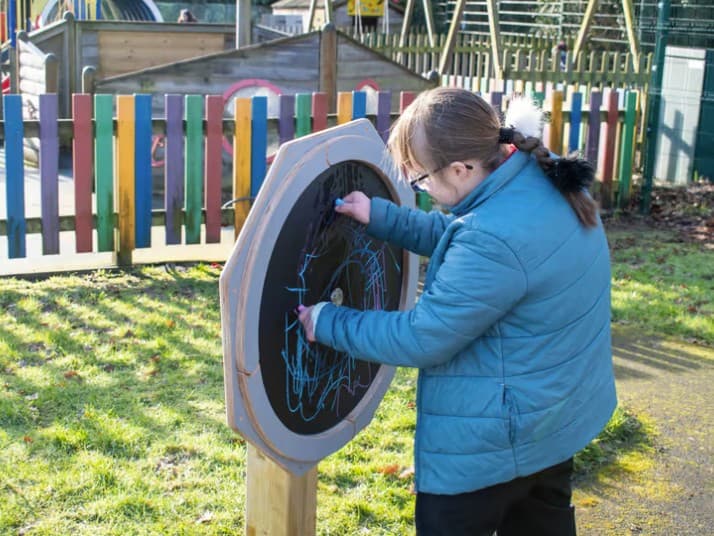 A child playing with a circular chalkboard, outside in a playground