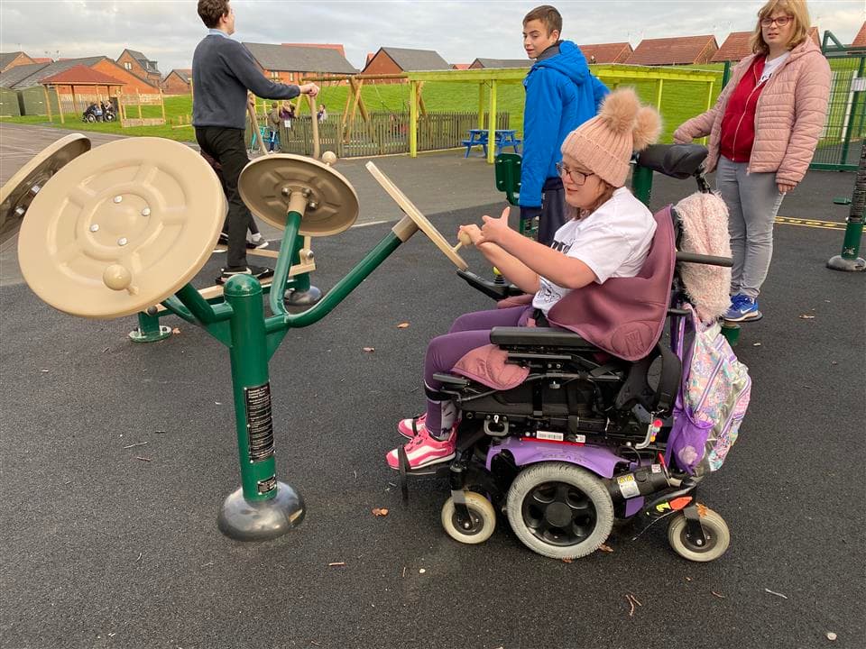 A girl in a wheelchair using one hand to move the tai chi spinner, a girl and two boys are stood behind her.