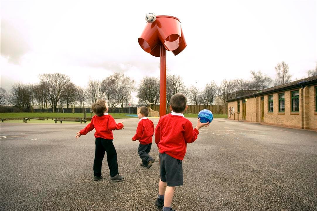 3 young boys throwing a ball into a red 4 way ball shoot, one boy is holding the ball.