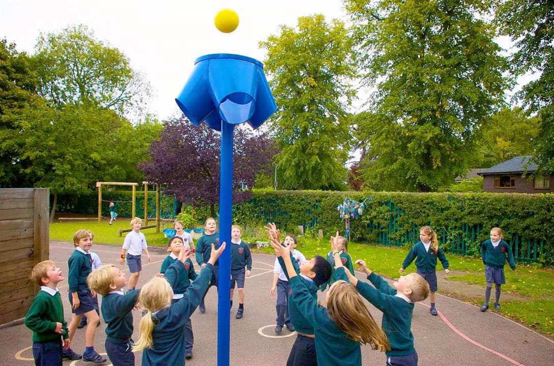 A class of children trying to throw and catch the ball into their 4 way ball shoot, the ball shoot is blue.