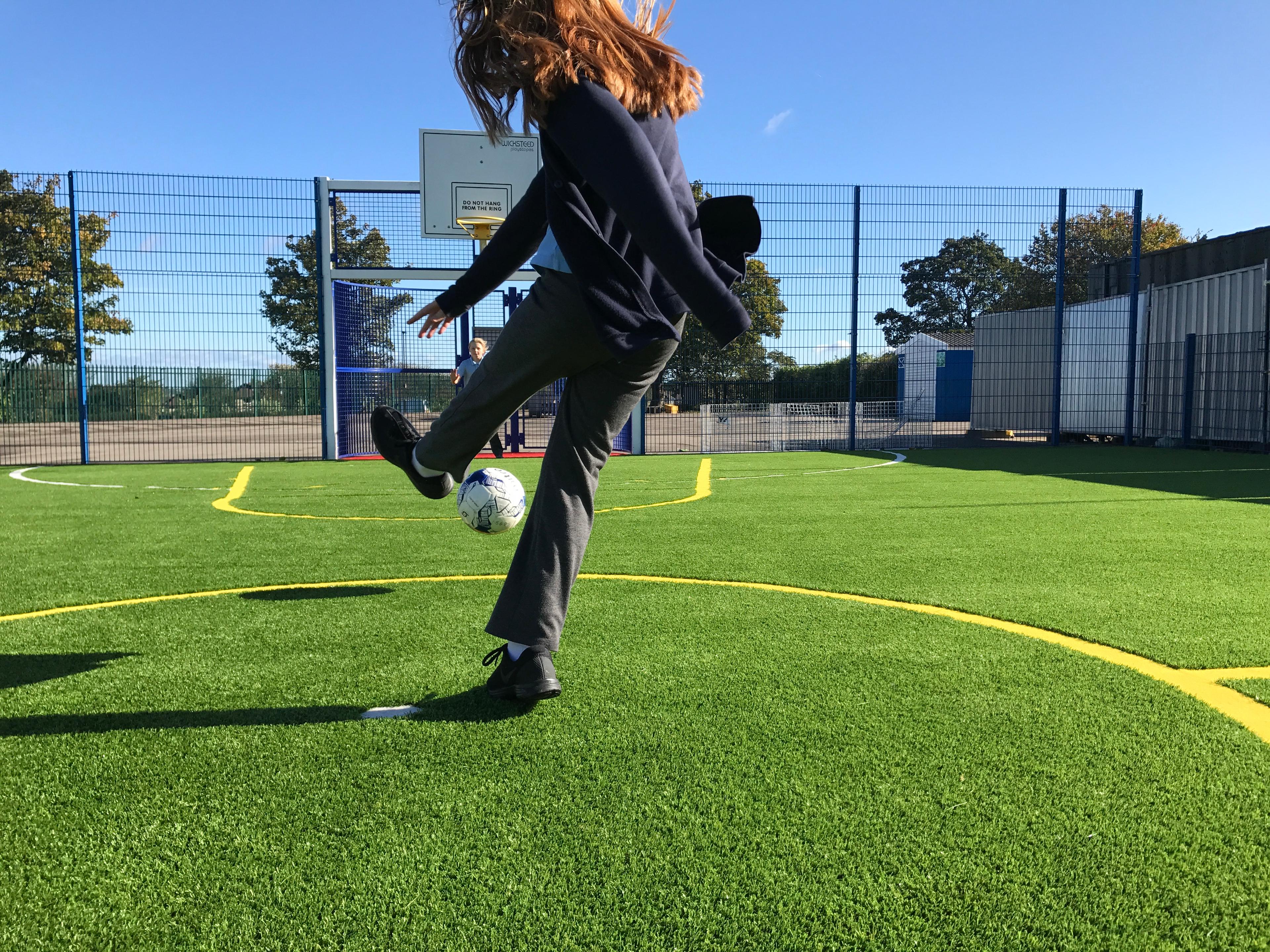 A girl taking a shot towards the goal on the multi-use games area at school. 
