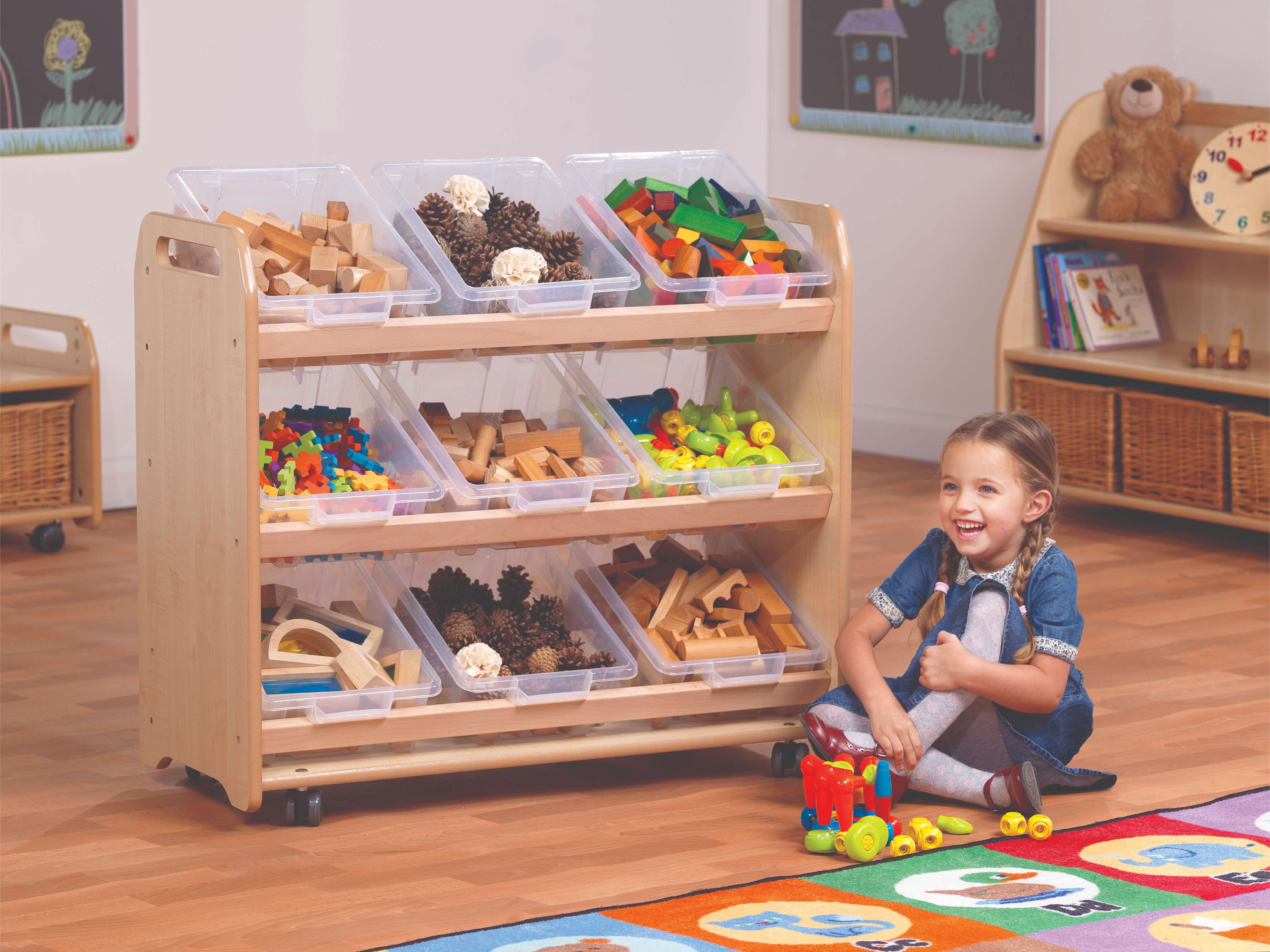 The Tilt Tote Storage with 9 Clear Tubs is full of different resources, a young girl is playing next to it in the classroom
