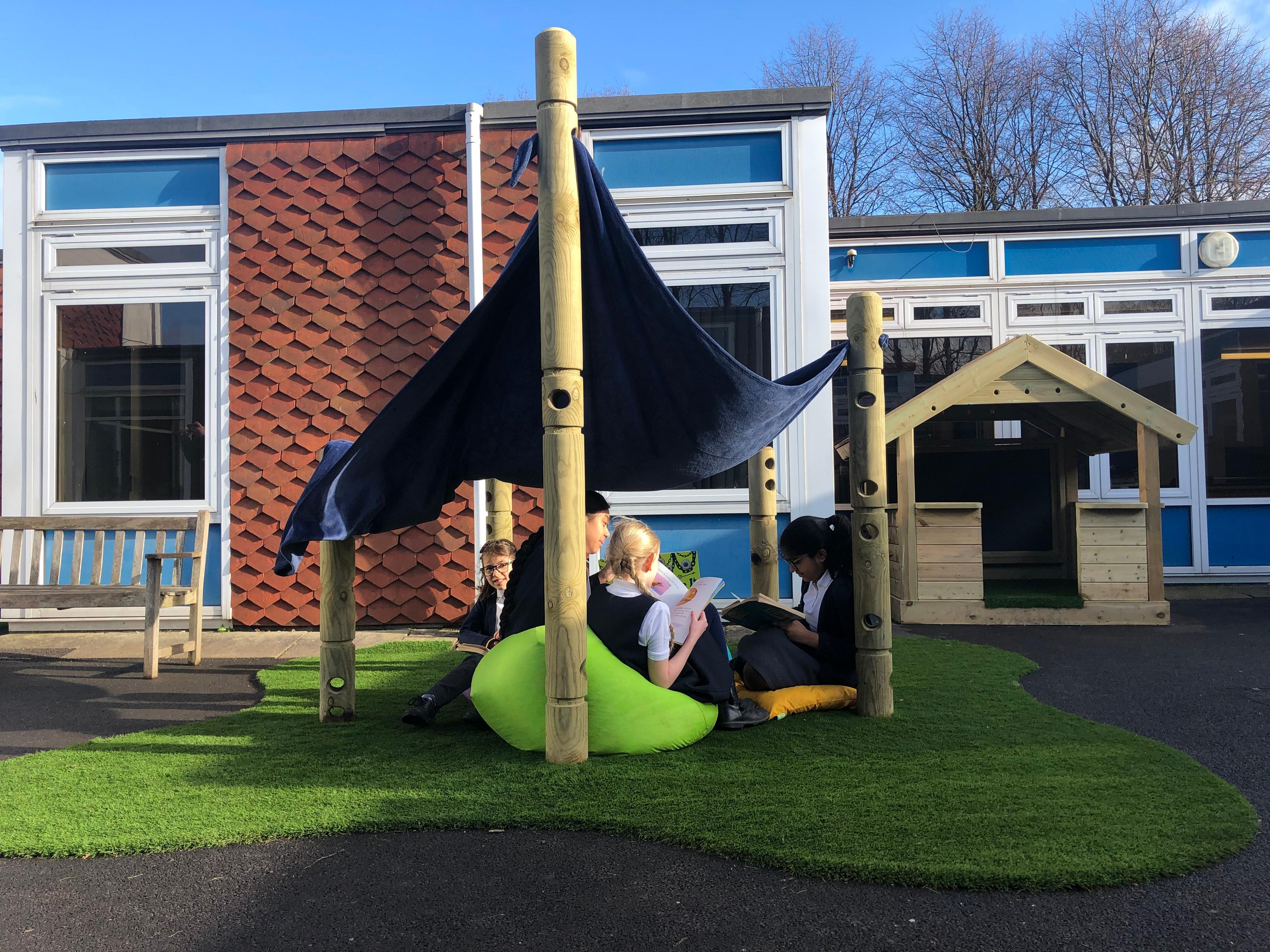 4 children sat underneath the den making post, they are sat on bean bags with a sheet on top of the den making posts creating a shelter.