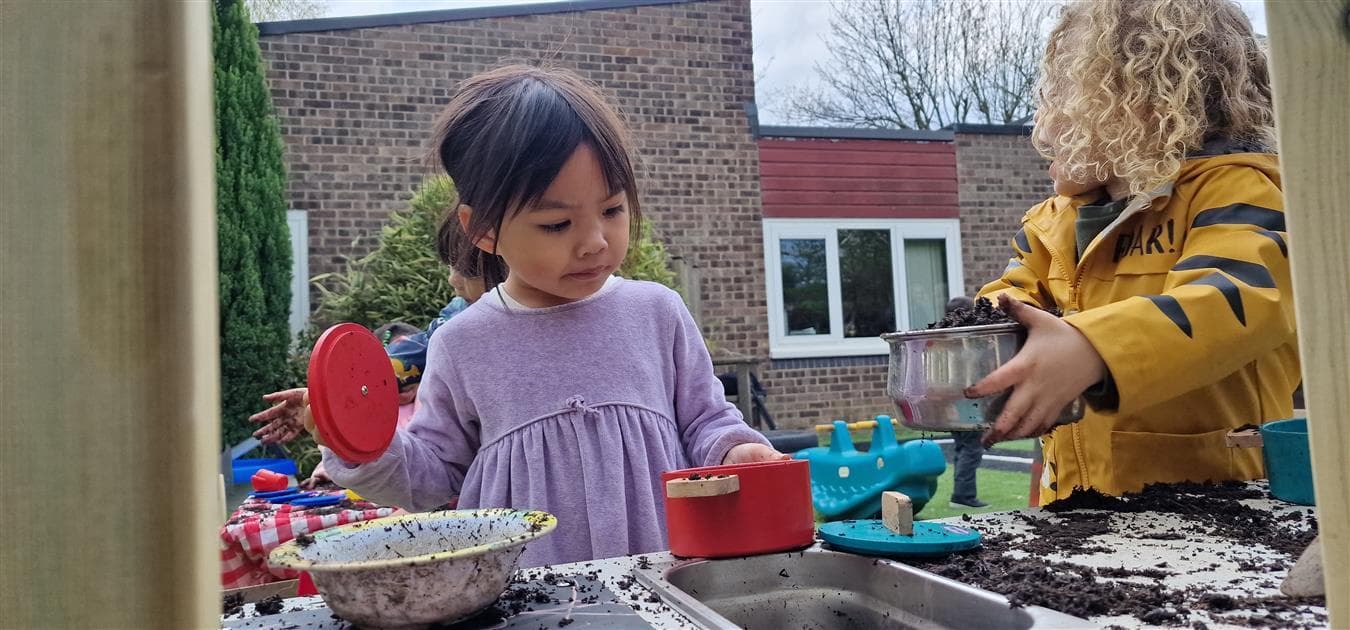 2 young children playing with the mud on their mud kitchen