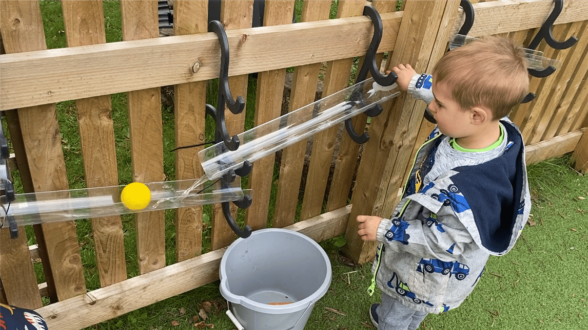 A young boy rolling a ball down the water channels that are connected to fencing
