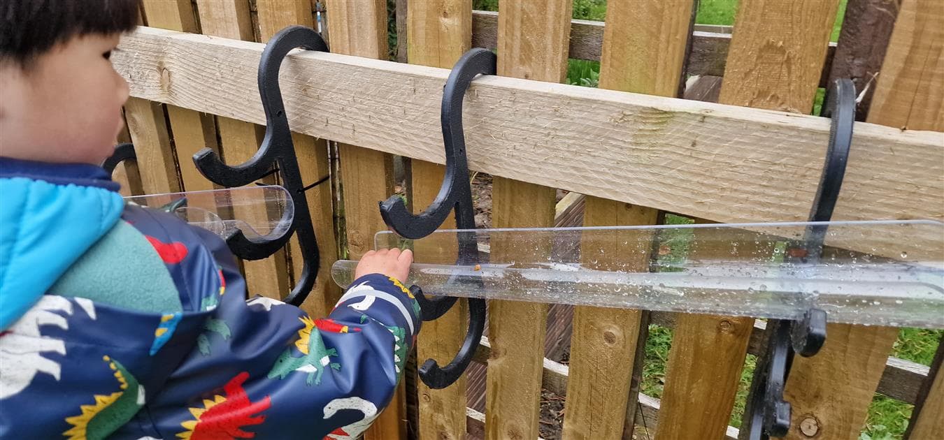 A young boy moving the water channels that are hooked onto the fence in their playground