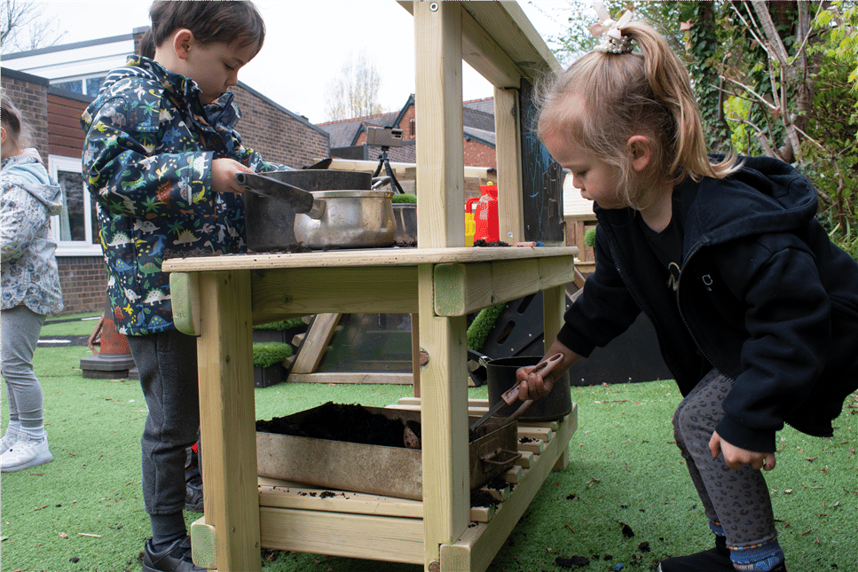 2 young children playing on the mud kitchen for there school