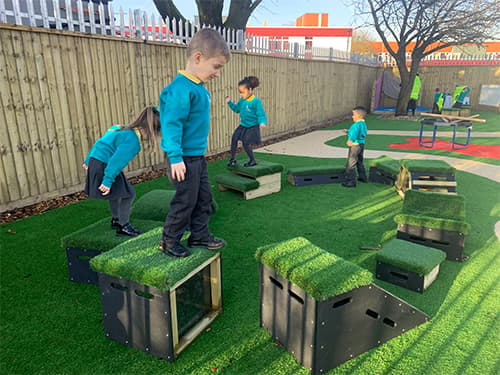 School children moving from one Get Set, Go! Block to others. The obstacle course has been placed on an artificial grass surface, with a path behind the course leading to another play area.
