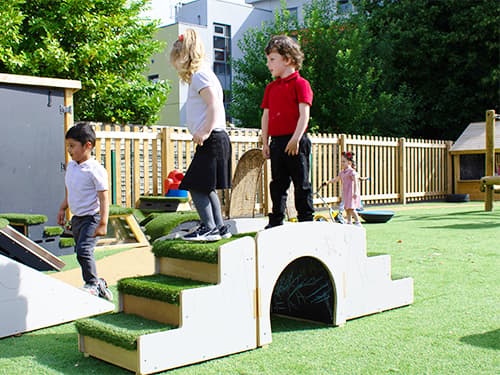 School children playing on Up and Under Blocks. Both the children are stood in the centre of the up and under block, with a variety of Get Set, Go! Blocks surrounding them.