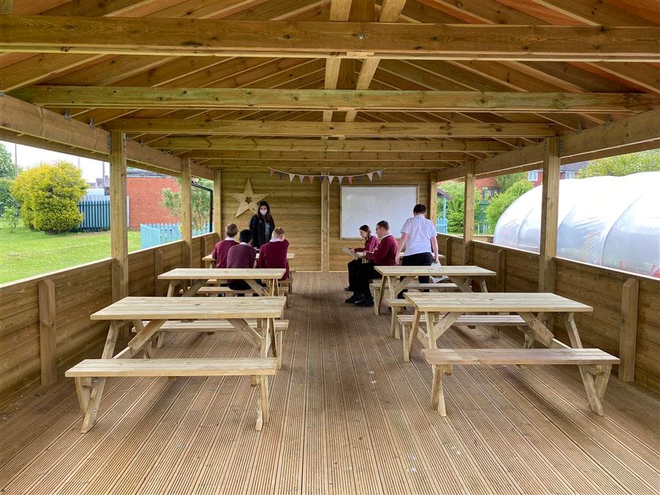 5 children sat on benches under their gable end, they are doing a lesson on the whiteboard at the front. 