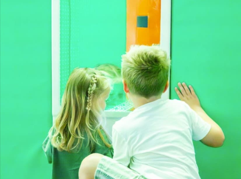 Two children looking at a brightly coloured panel on a green wall