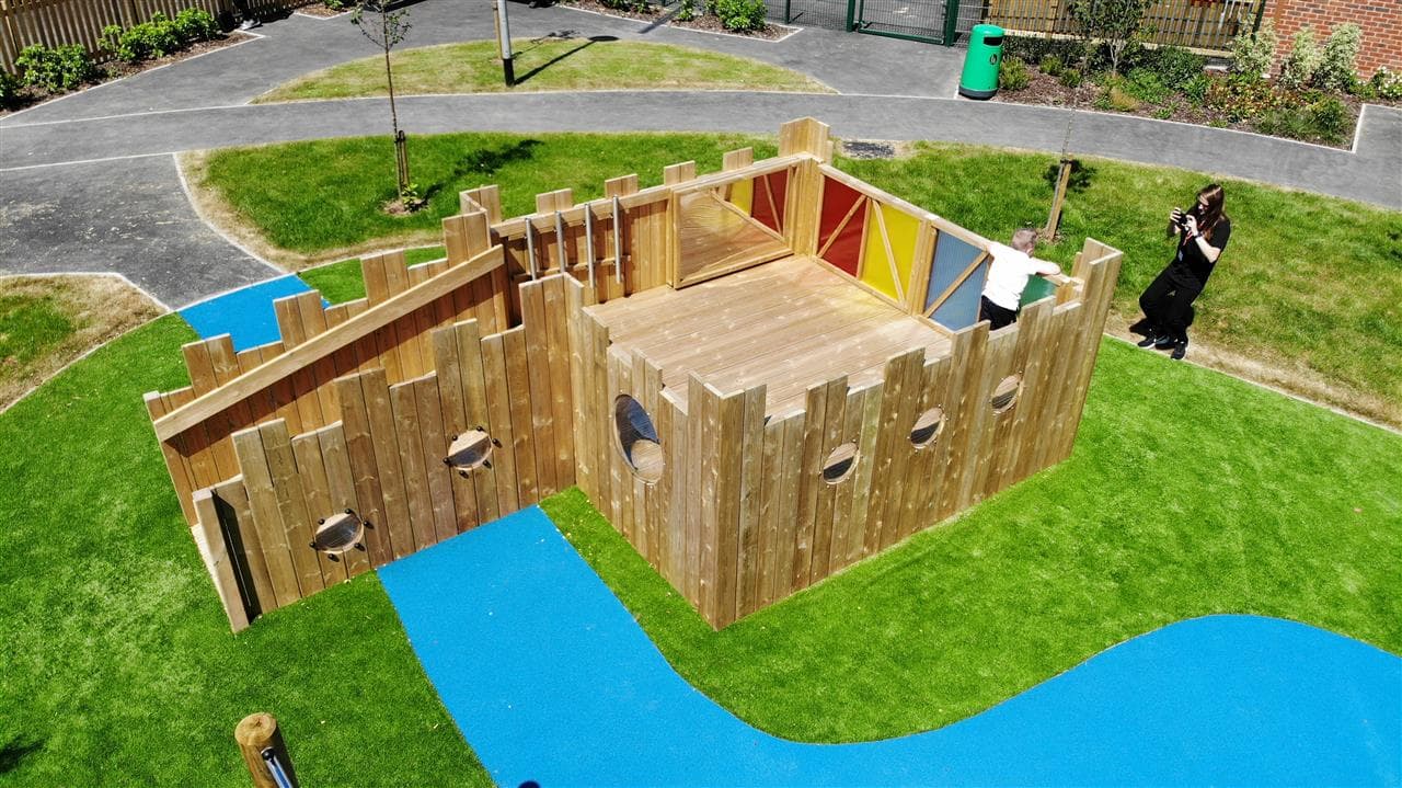 A birds eye view of children playing on the play tower, there are coloured sensory panels around the tower, with a ramp leading up to it.