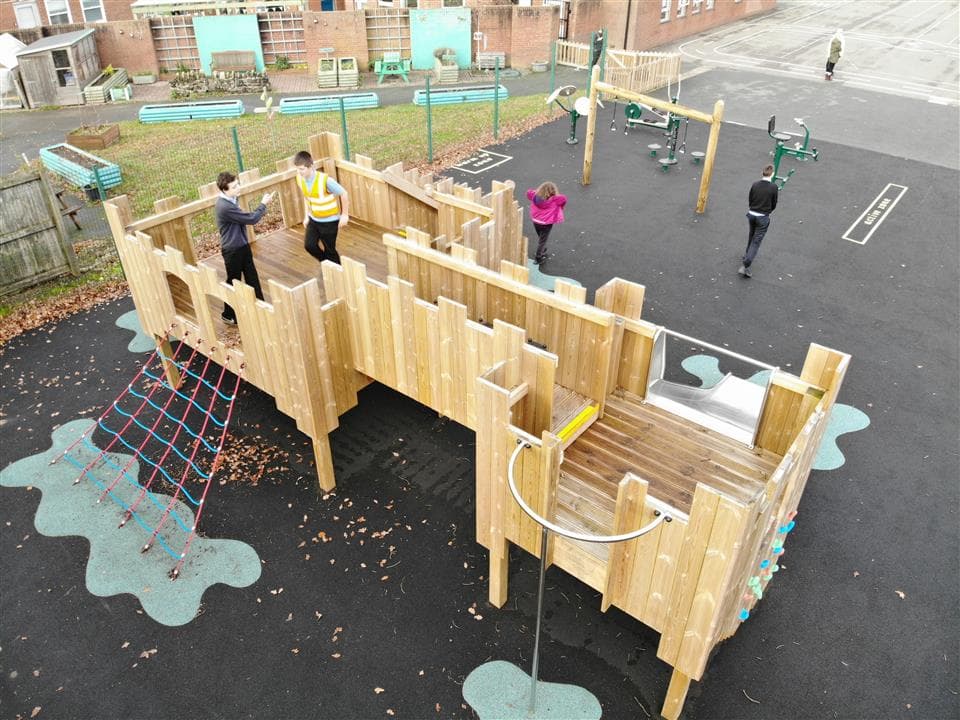 a few children playing on their play castle, there is one young boy stood on top and the rest of the children are stood around.