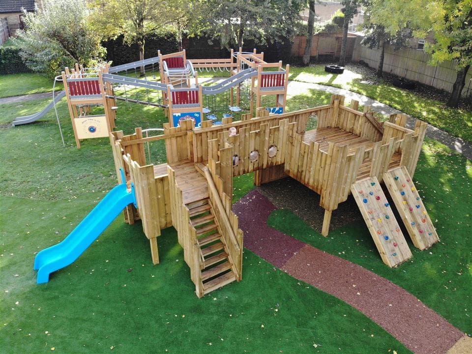 A birds eye view of children playing on their play castle, the play castle is surrounded by artificial grass.