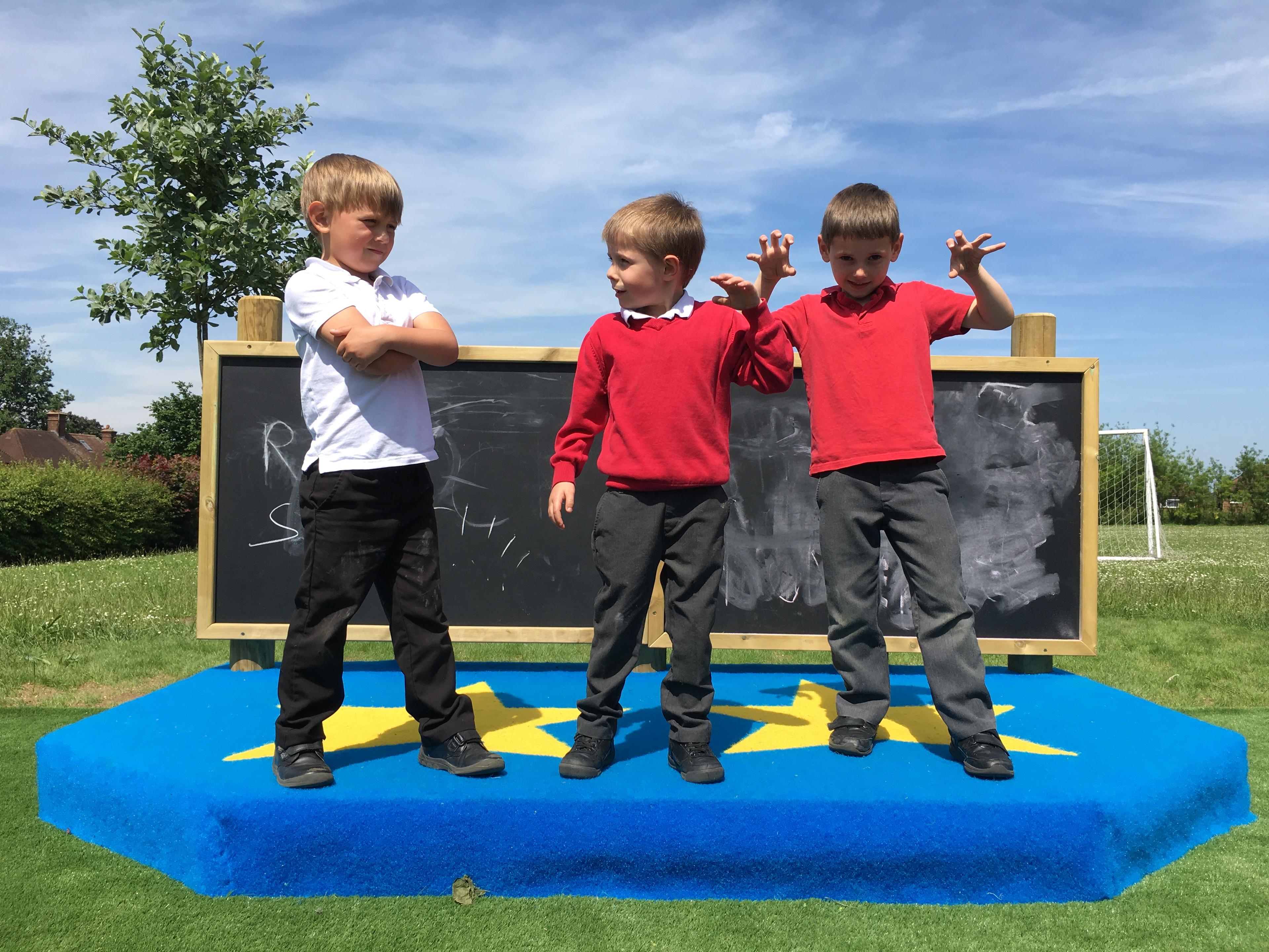 3 young boys playing on our performance stage, a giant chalk board which is part of the performance stage is in the background behind the boys.