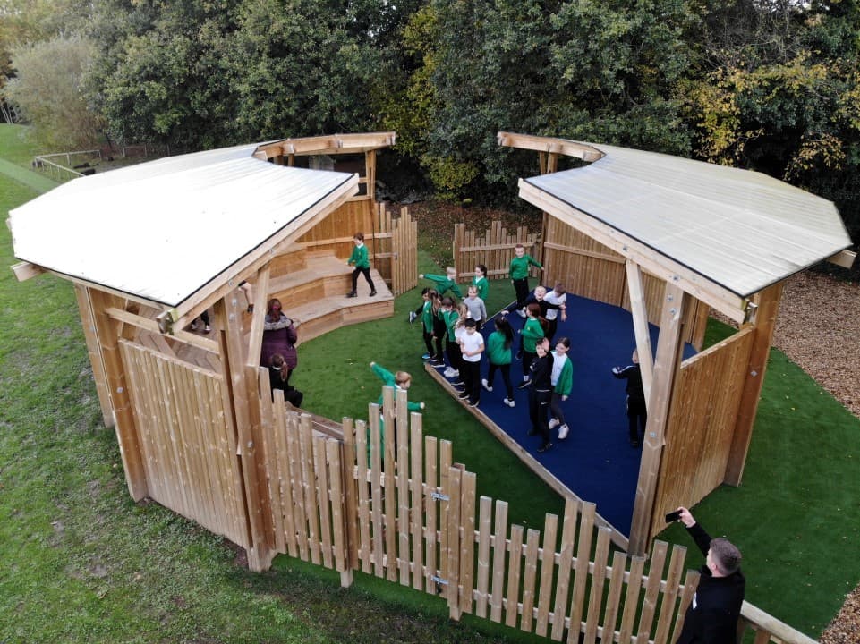 a birdseye view of a timber ampitheatre with ceiling and children gathered within chatting and playing