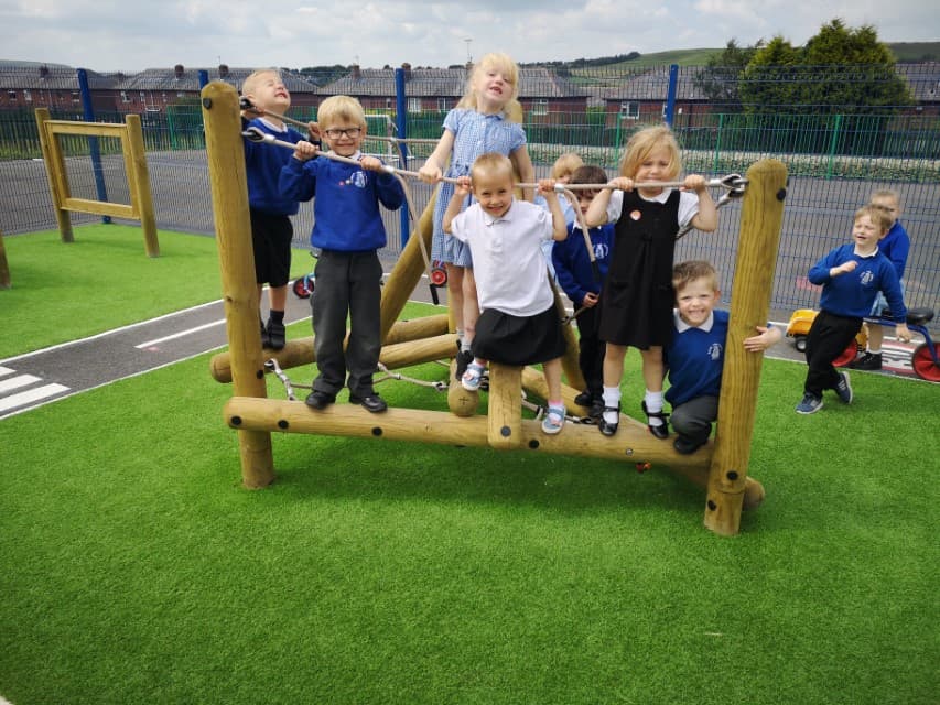 A Playframe has been installed on artificial grass, with a wetpour road going around the area. A group of children are playing on the climbing frame, as other children are running over to it.