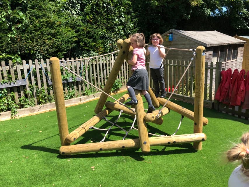 A Playframe has been installed on top of artificial grass. A couple of children are playing on the climbing frame, with a wooden fence going around the area.
