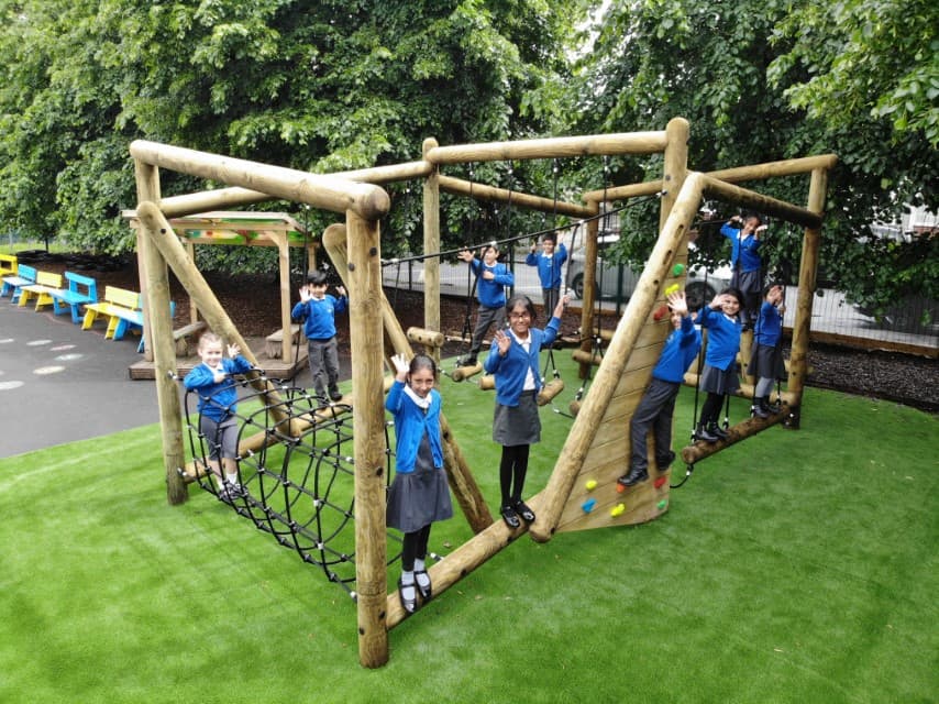 A Forest Circuit installed on artificial grass, with a group of children playing on the equipment. Around the Forest Circuit, there's a wetpour play area and a lot of trees.