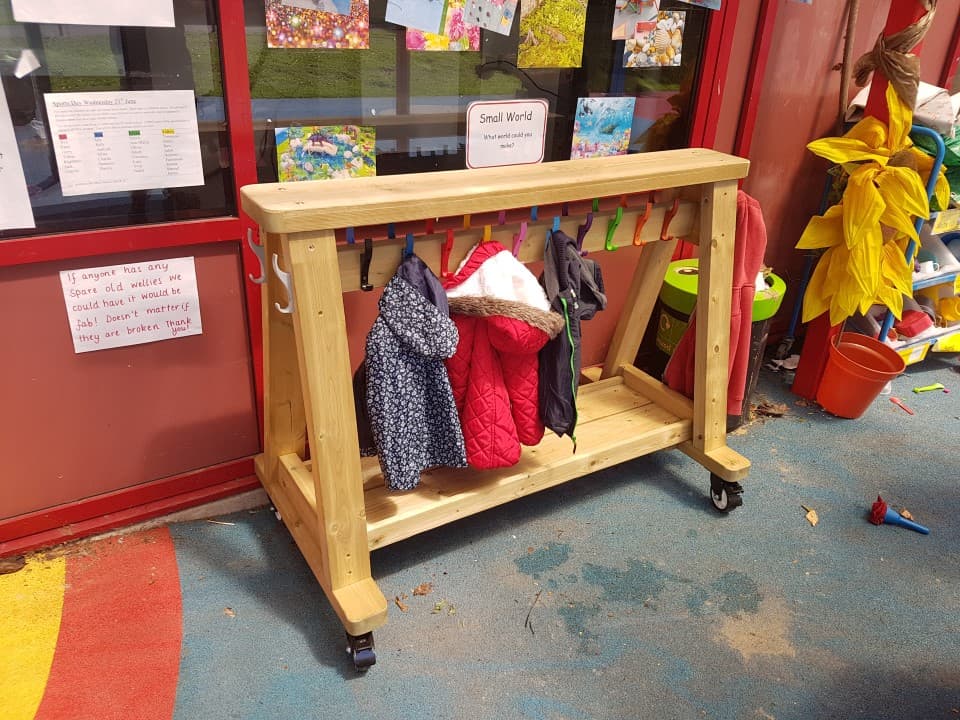 a timber coat rack on wheels with rainbow hooks and little coats hung on them outside a nursery