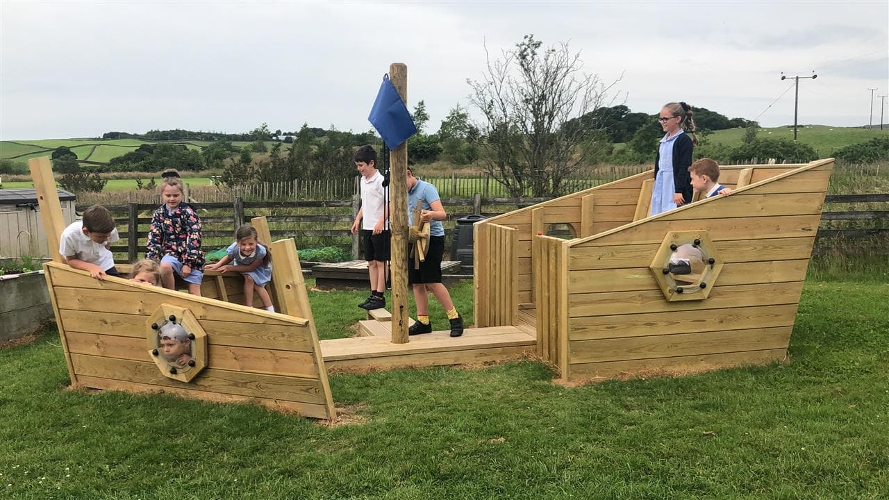 9 children playing on our play ship, one boy is stirring the ship and one young boy is looking through the bubble window.