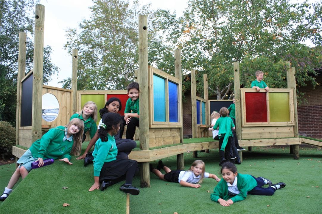 9 children sitting and playing on their new imagination station, 2 children are lying on the artificial grass