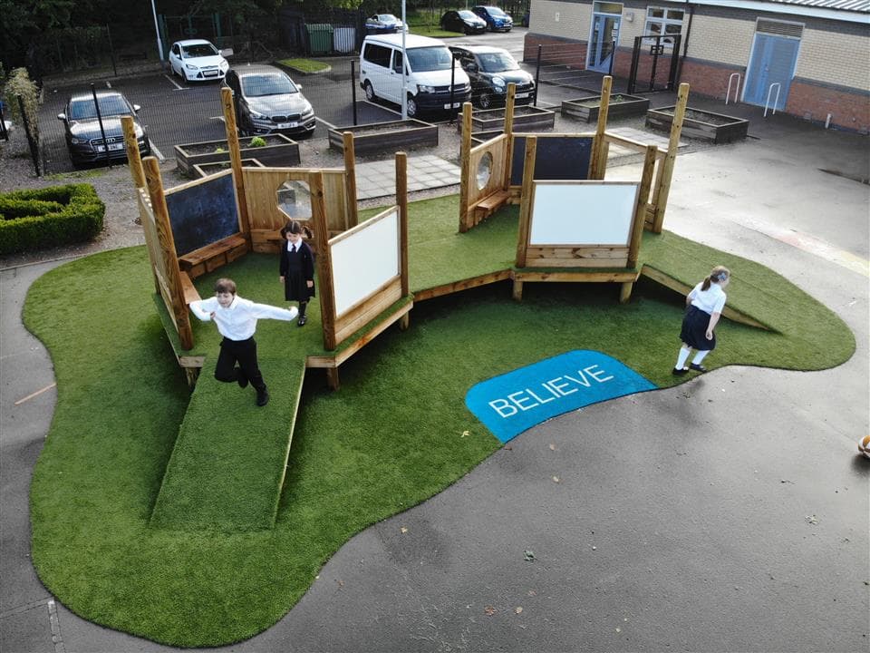 3 children playing on our imagination station, 2 are on the equipment and 1 is walking on the artificial grass.
