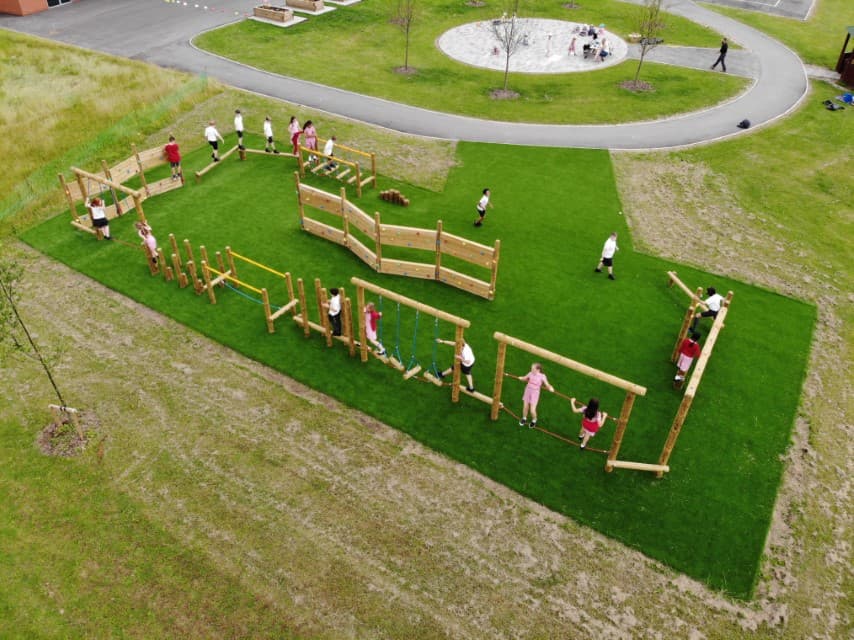 A birds eye view of a class of children playing on their trim trail, artificial grass covers surrounds this area.