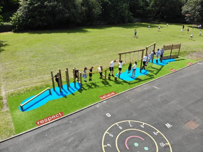 A birds eye view of a class of children playing on their trim trail, artificial grass and positive Saferturf signs are scattered around the edges.