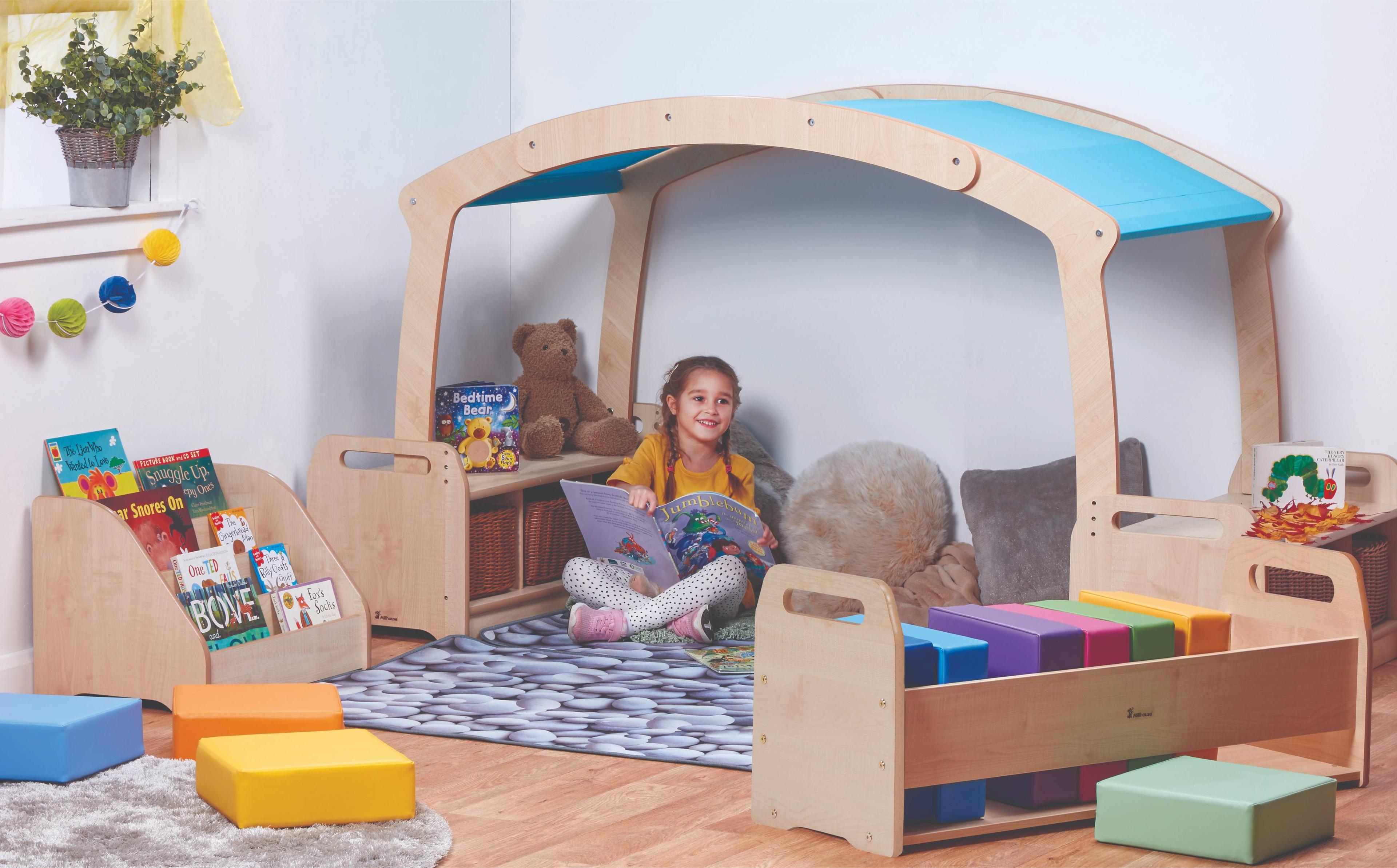 A young girl reading a book in the Mini Rainbow Reading Zone with Baskets, in a classroom