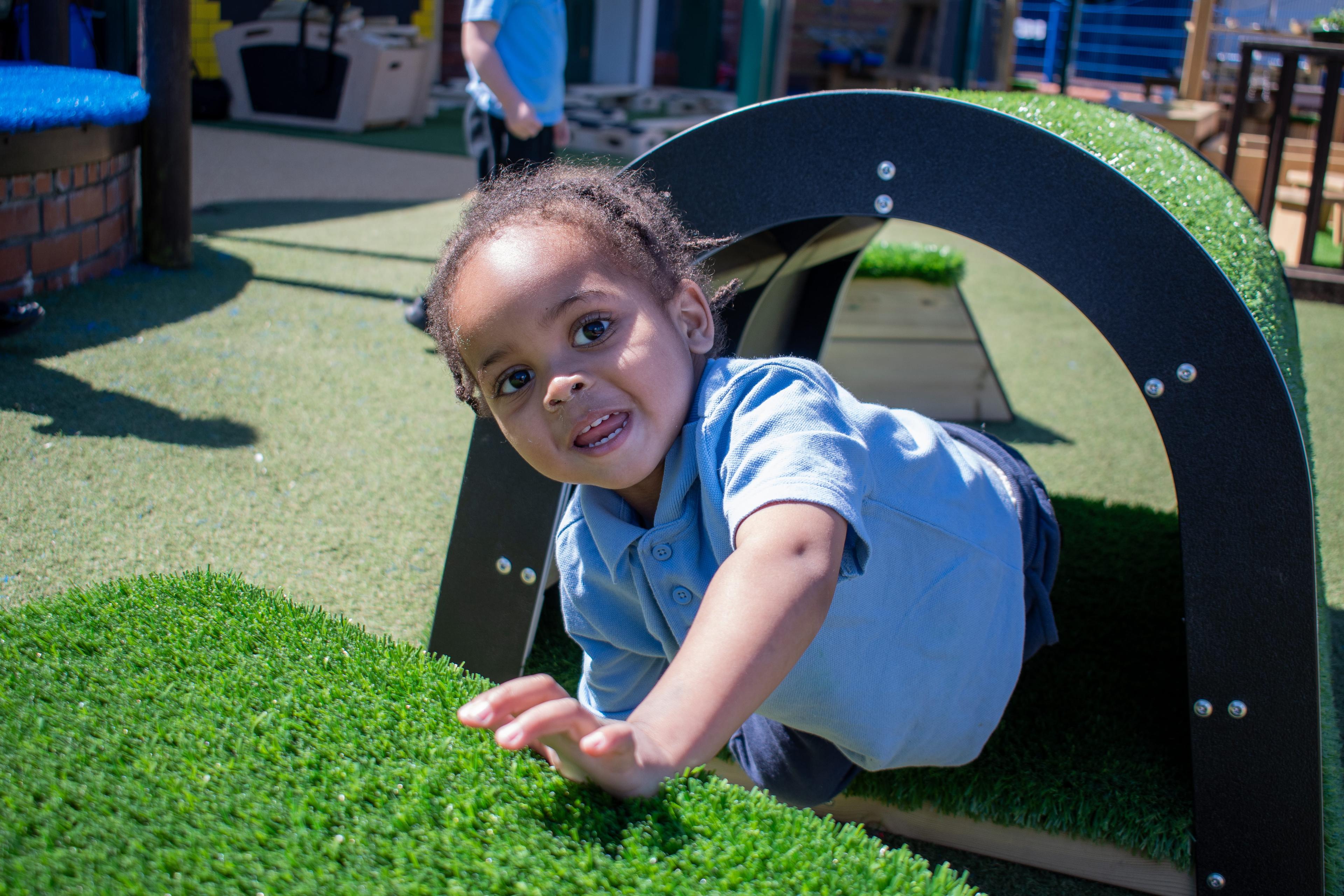 A little girl is climbing through the tunnel block and is smiling at the camera.
