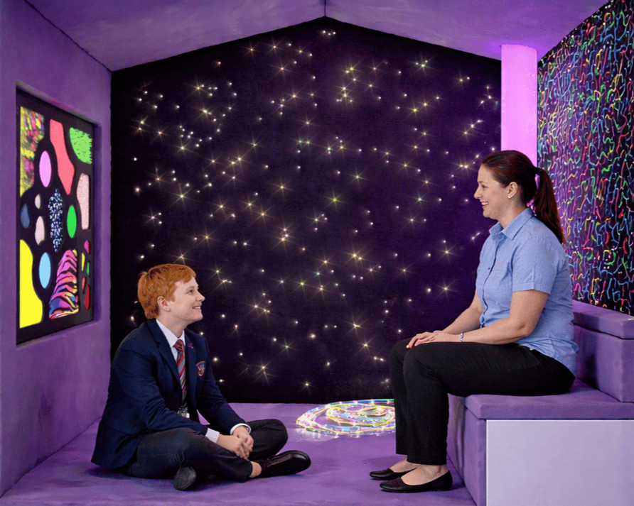 A teacher and a high school student are sat inside a sensory nook, talking to each other.