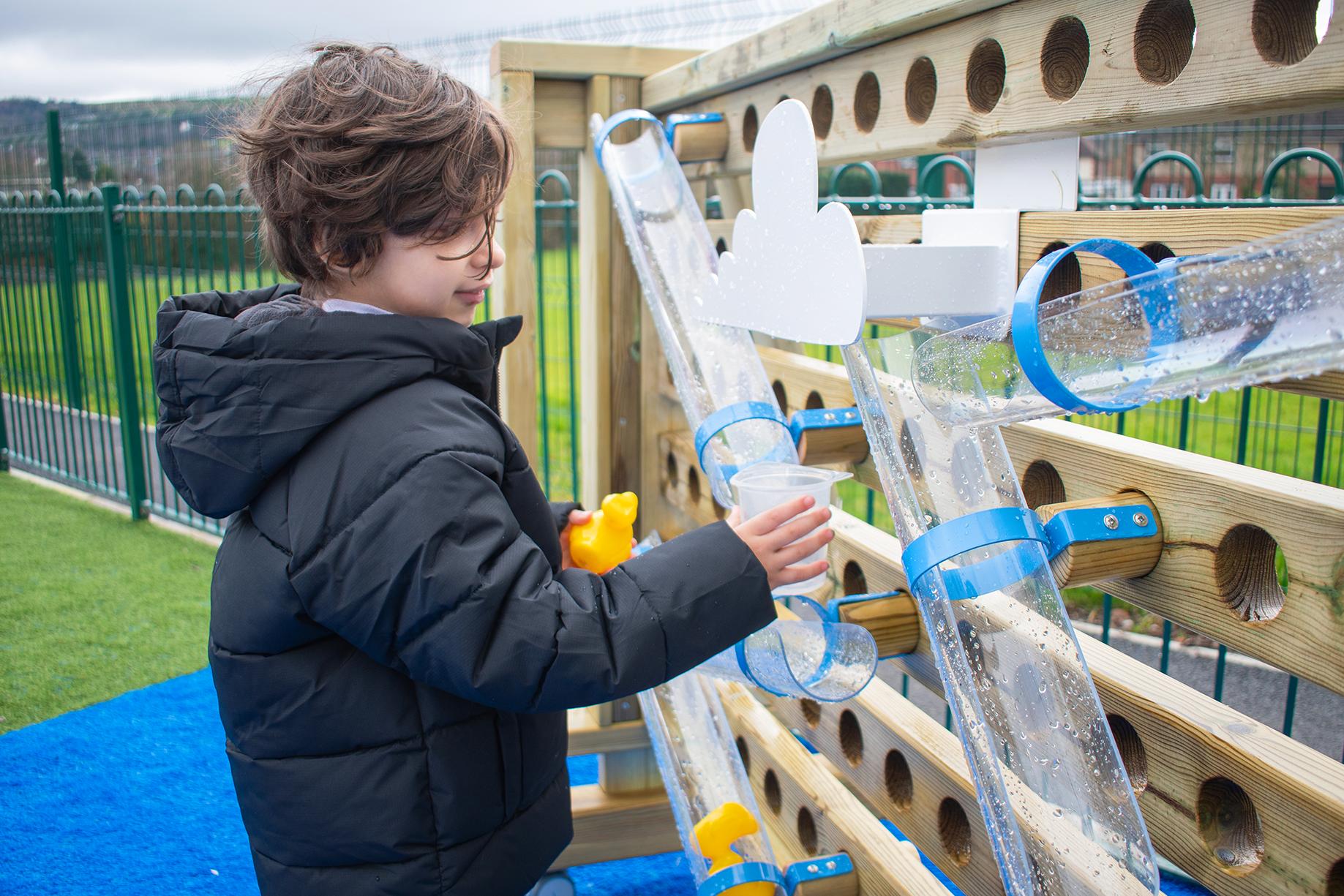 A boy holding a yellow toy duck. Reconfiguring the water channels to direct the flow of the water