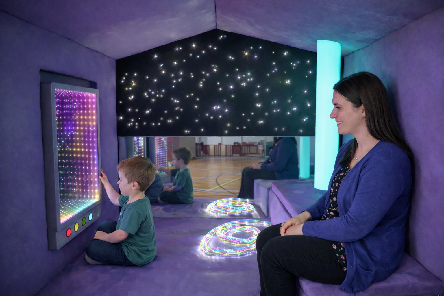 A teacher and a little child are sat inside the Sensory Nook. The child is interacting with different elements as the teacher watches.