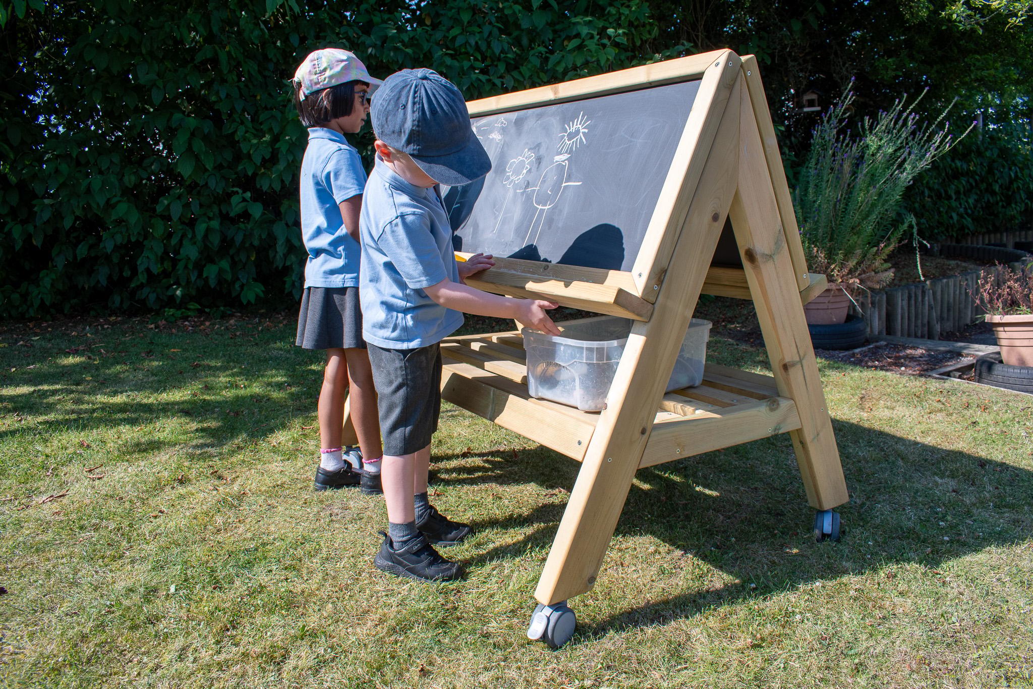 Children picking up chalk from shelf under Easel on Wheels