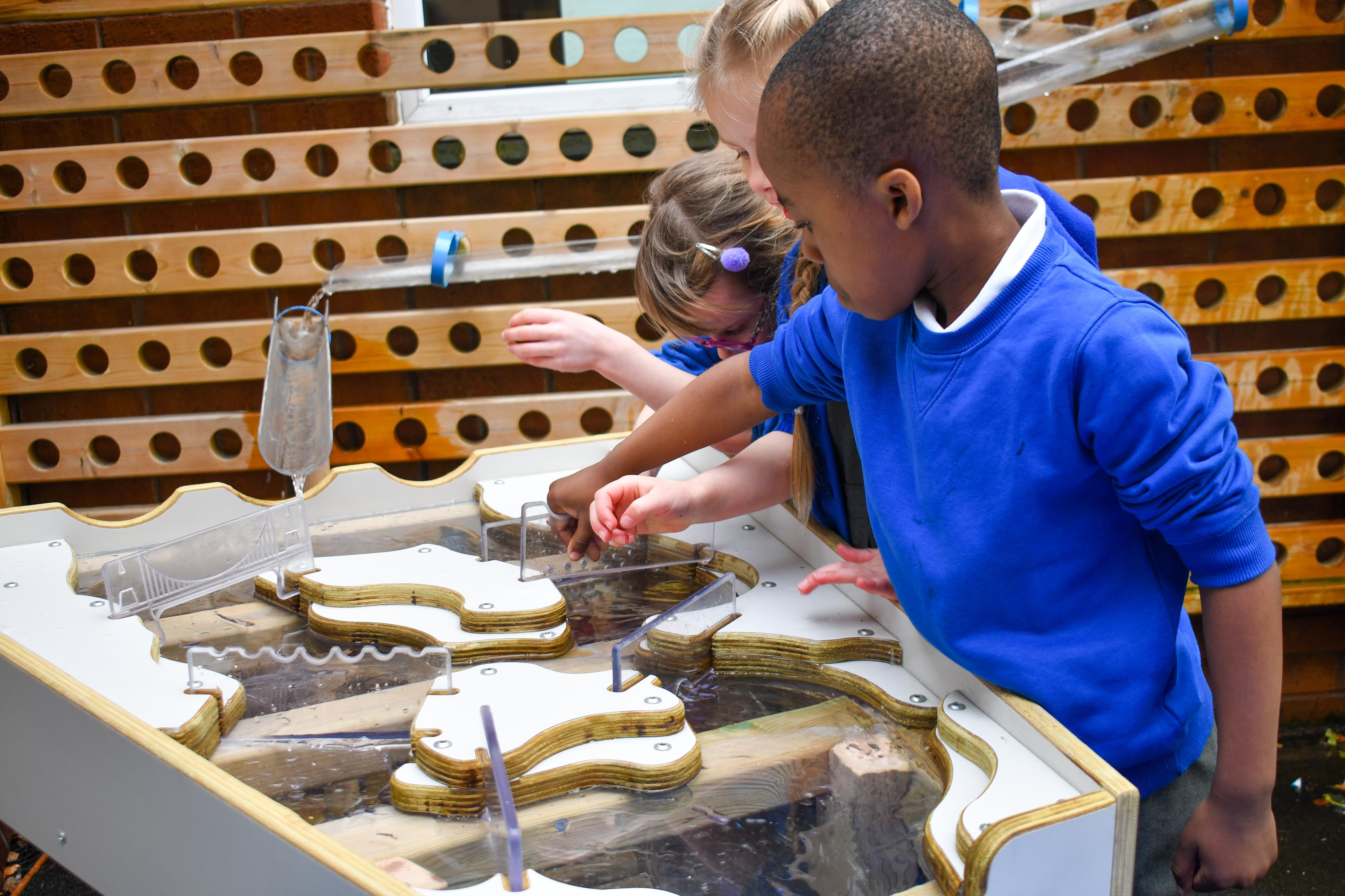 A close up of the damming station being used with the water wall. Three children are moving the dividers to let water flow through