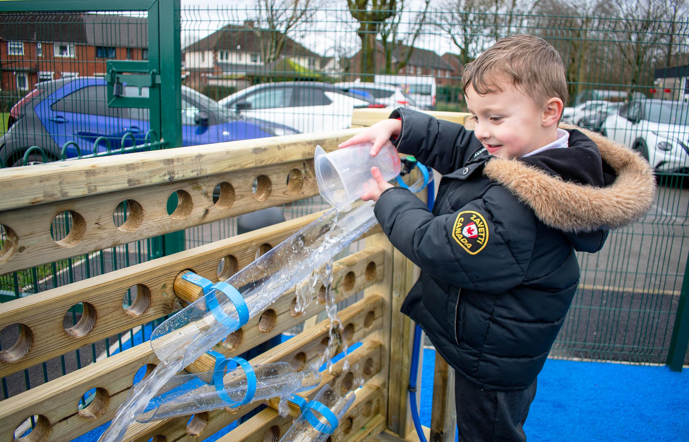 A happy boy reaching to the top of the movable water wall to pour water out of a plastic jug into water channels
