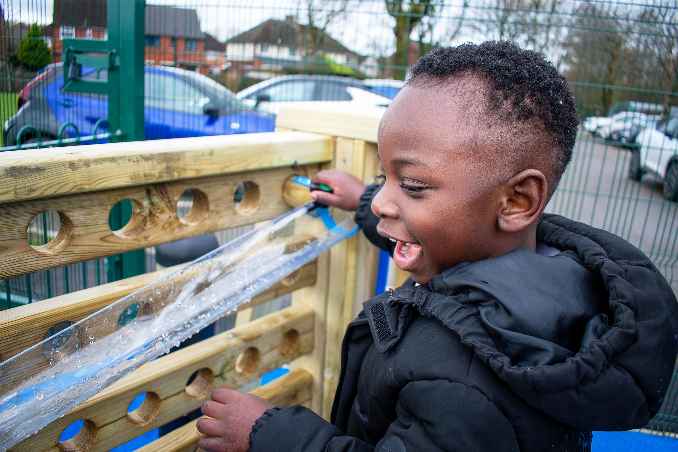 A boy with a big smile on his face, turning on the hose for the movable water wall and seeing water pour out