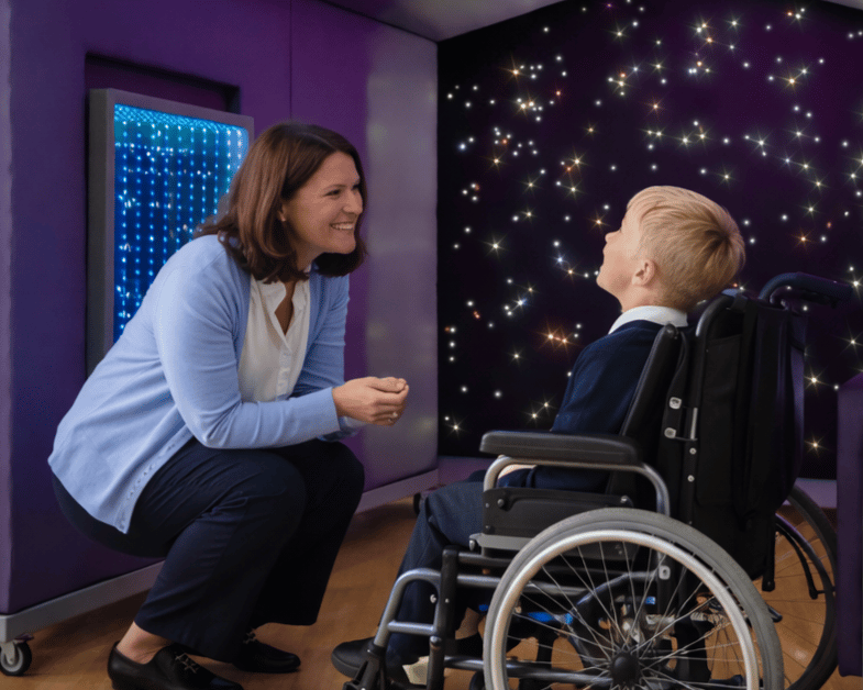 A teacher is squatting beside a child in a wheelchair, as they both explore the large Sensory Shelter.