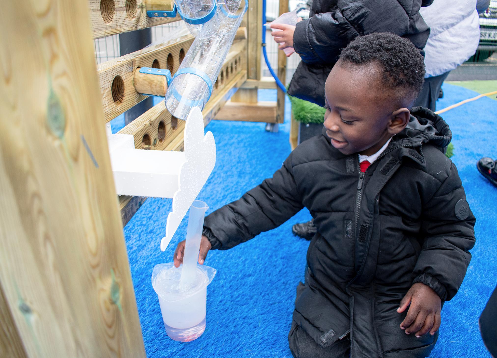 A boy collecting water from the water cloud at the bottom of the movable water wall with a plastic container