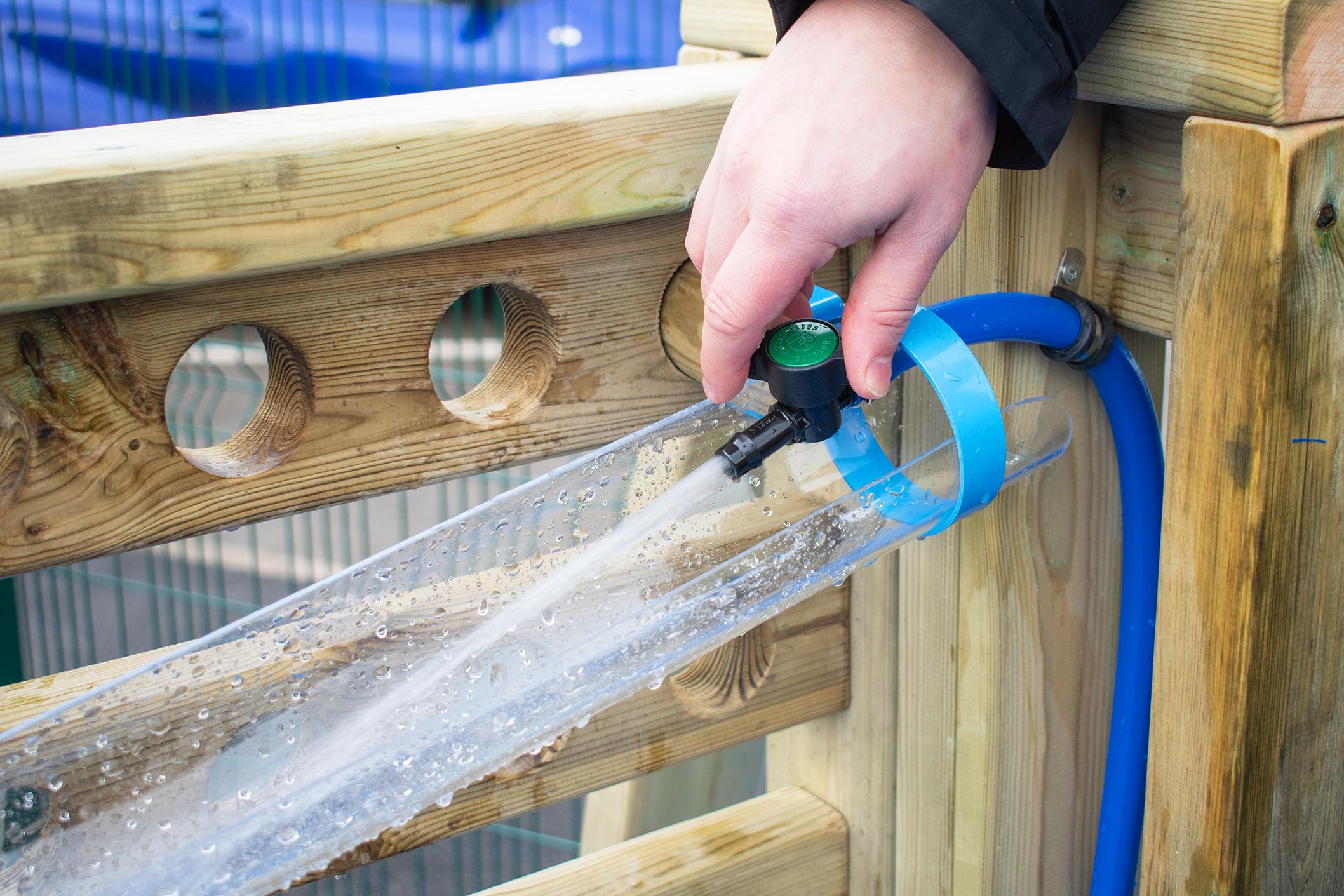 A close up image of a hose being fed through the movable water wall to flow water into the water channels